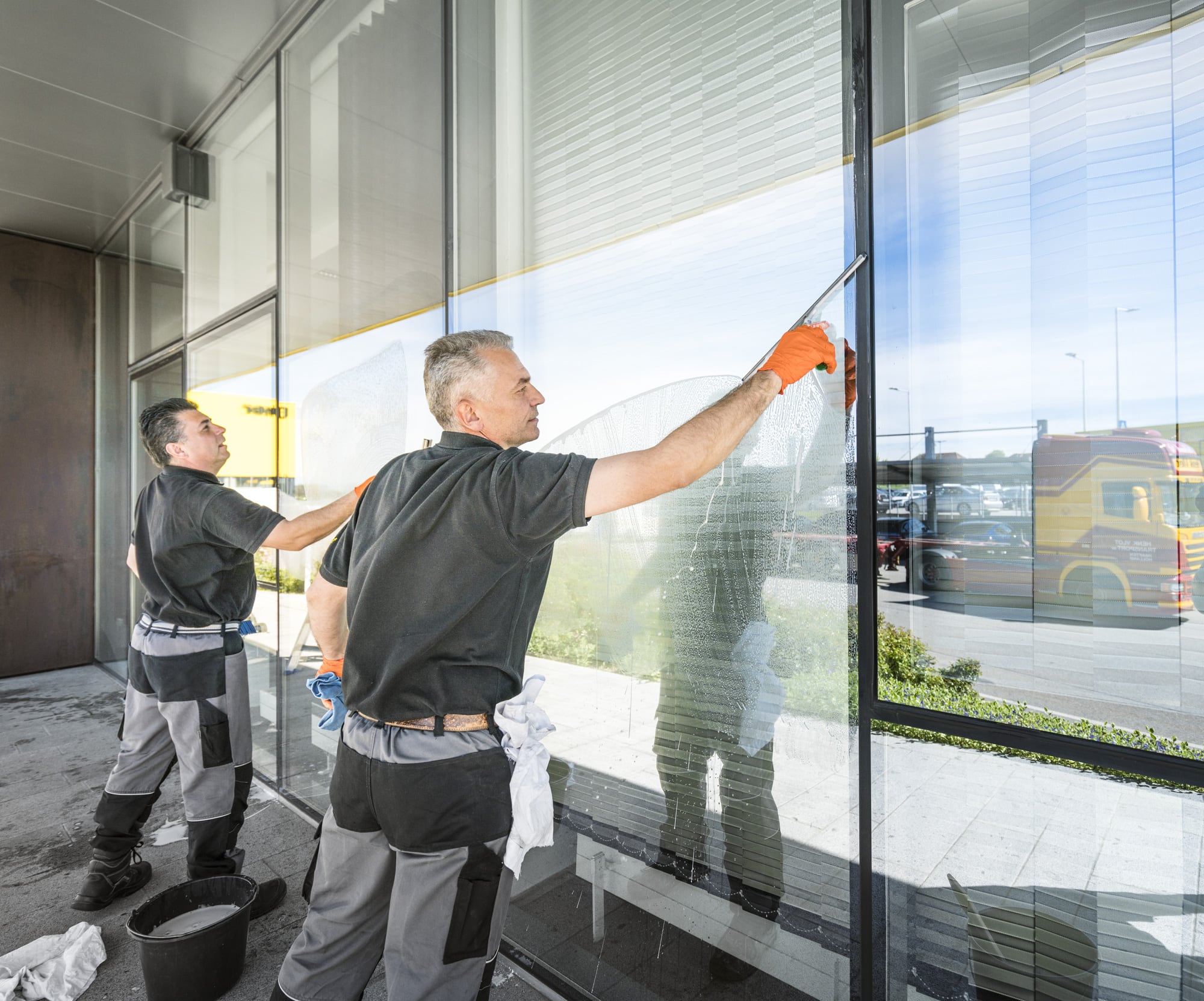 Zwei Arbeiter putzen ein Fenster einer Glasfront mit Fensterabzieher