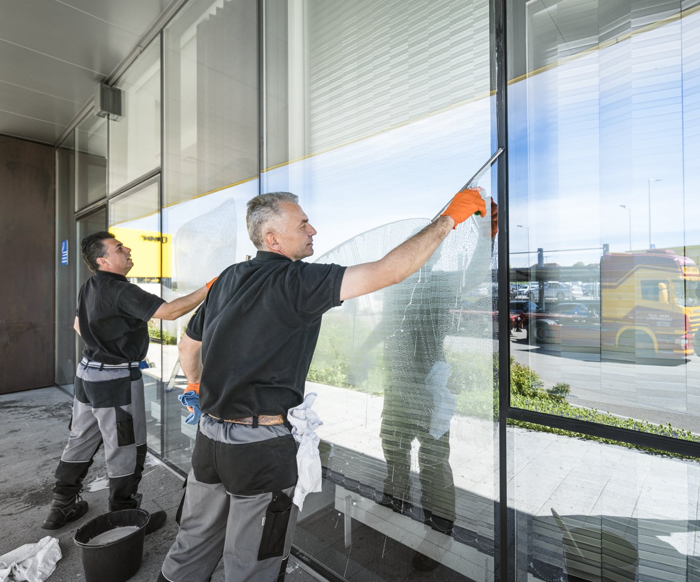 Zwei Arbeiter putzen ein Fenster einer Glasfront mit Fensterabzieher